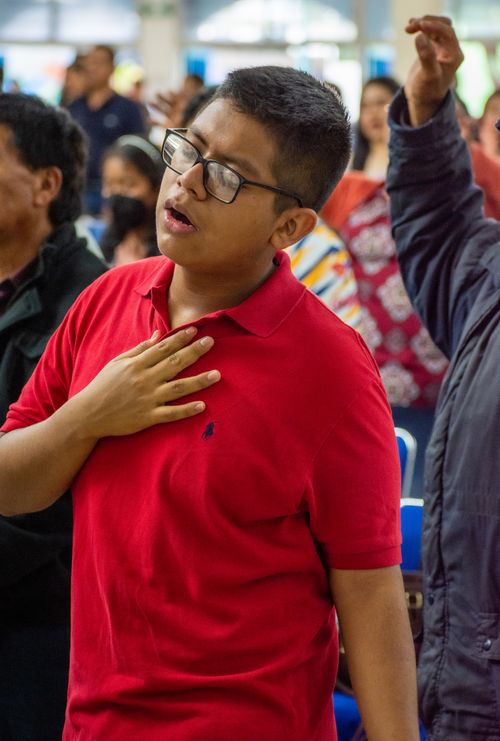 Free Adult man with short hair and glasses, eyes closed, hand on chest, appears to be praying indoors. Stock Photo