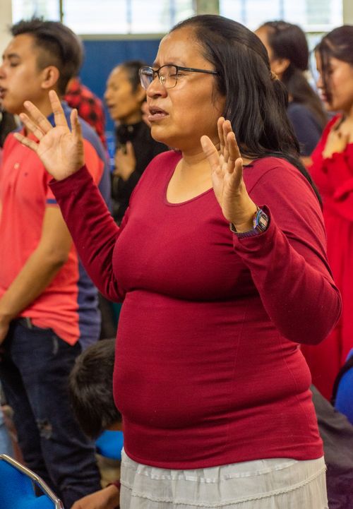 Free A woman in a red shirt stands with eyes closed and hands raised in prayer during a gathering. Stock Photo