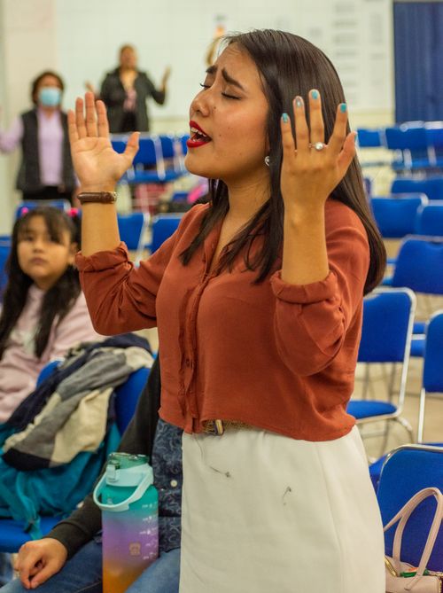 Free Woman with raised hands and closed eyes singing passionately at an indoor gathering. Stock Photo