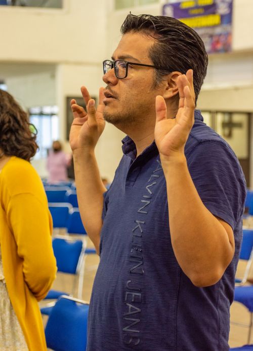 Free A contemplative man stands in meditation, hands raised in prayer during an indoor gathering. Stock Photo