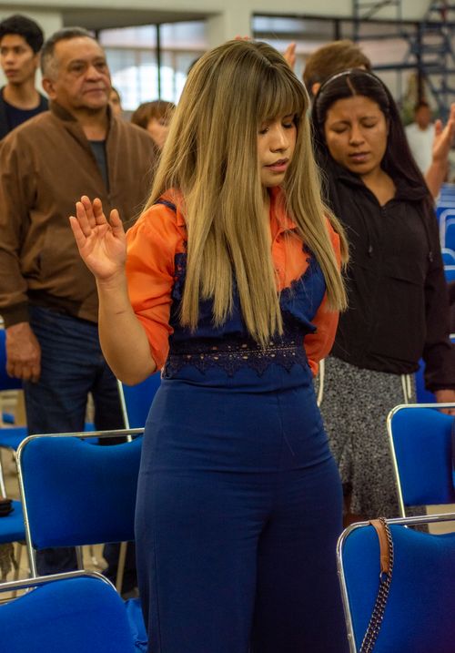 Free A woman with long blond hair and closed eyes prays during a church service, standing among seated attendees. Stock Photo