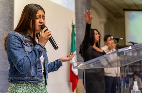 Free A young woman sings passionately on stage during a church service with others in prayer. Stock Photo