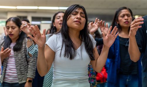 Free Group of young women raising hands in worship during a religious event indoors. Stock Photo