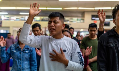 Free Diverse group engaging in spiritual worship, hands raised in prayer and unity indoors. Stock Photo