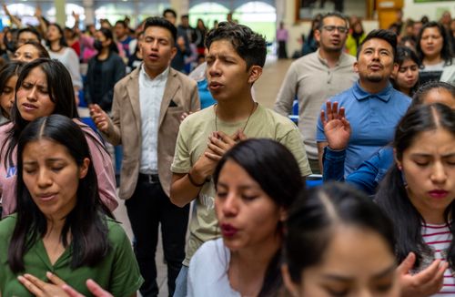 Free Young adults engaged in spiritual worship at an indoor event, expressing devotion. Stock Photo