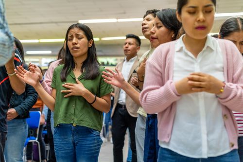 Free A diverse group of people standing indoors, engaging in collective prayer with closed eyes and devotional expressions. Stock Photo