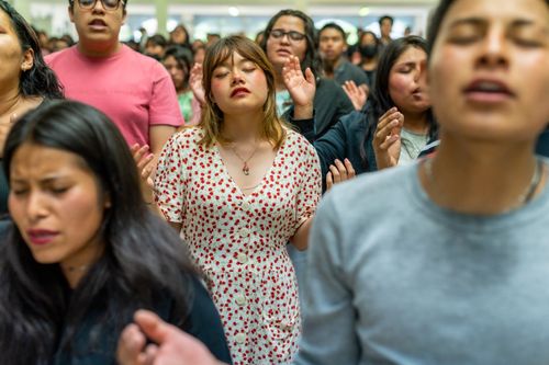 Free A diverse group of people with eyes closed and hands raised participate in a heartfelt communal prayer indoors. Stock Photo