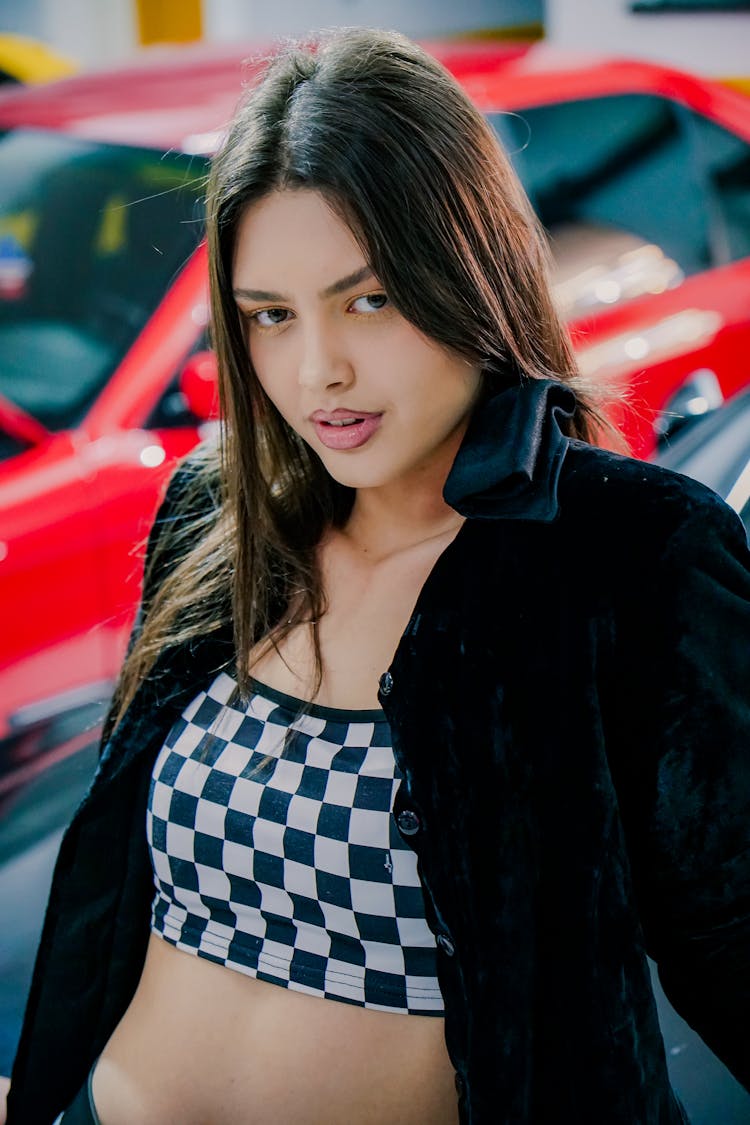 Young Woman In A Checkered Crop Top Standing In A Garage With Cars 