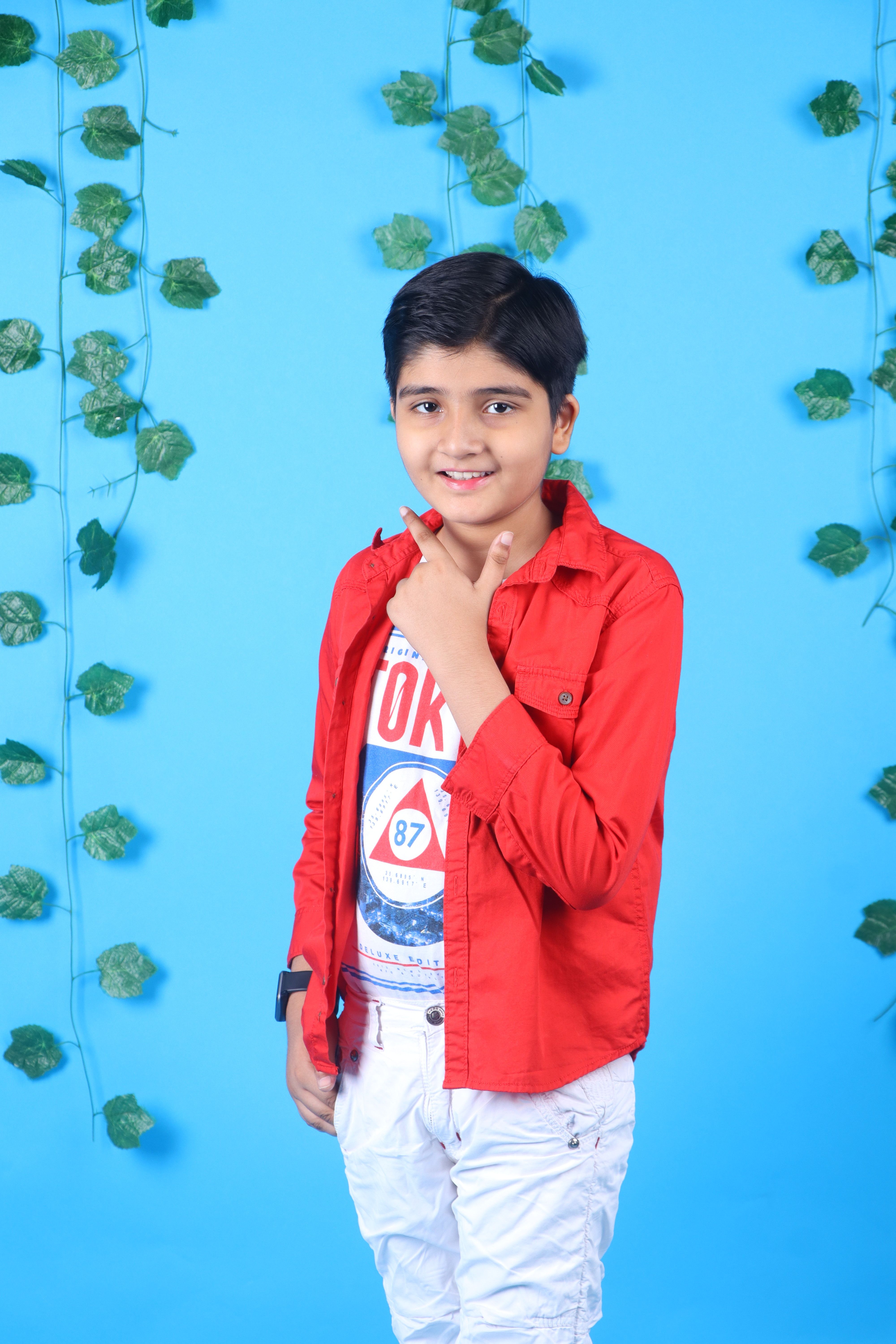 Smiling boy in a vibrant red shirt against a leaf-decorated blue wall.