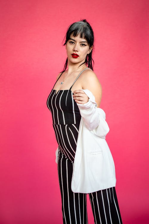 Young Woman in a Striped Jumpsuit Posing in Studio on Pink Background 