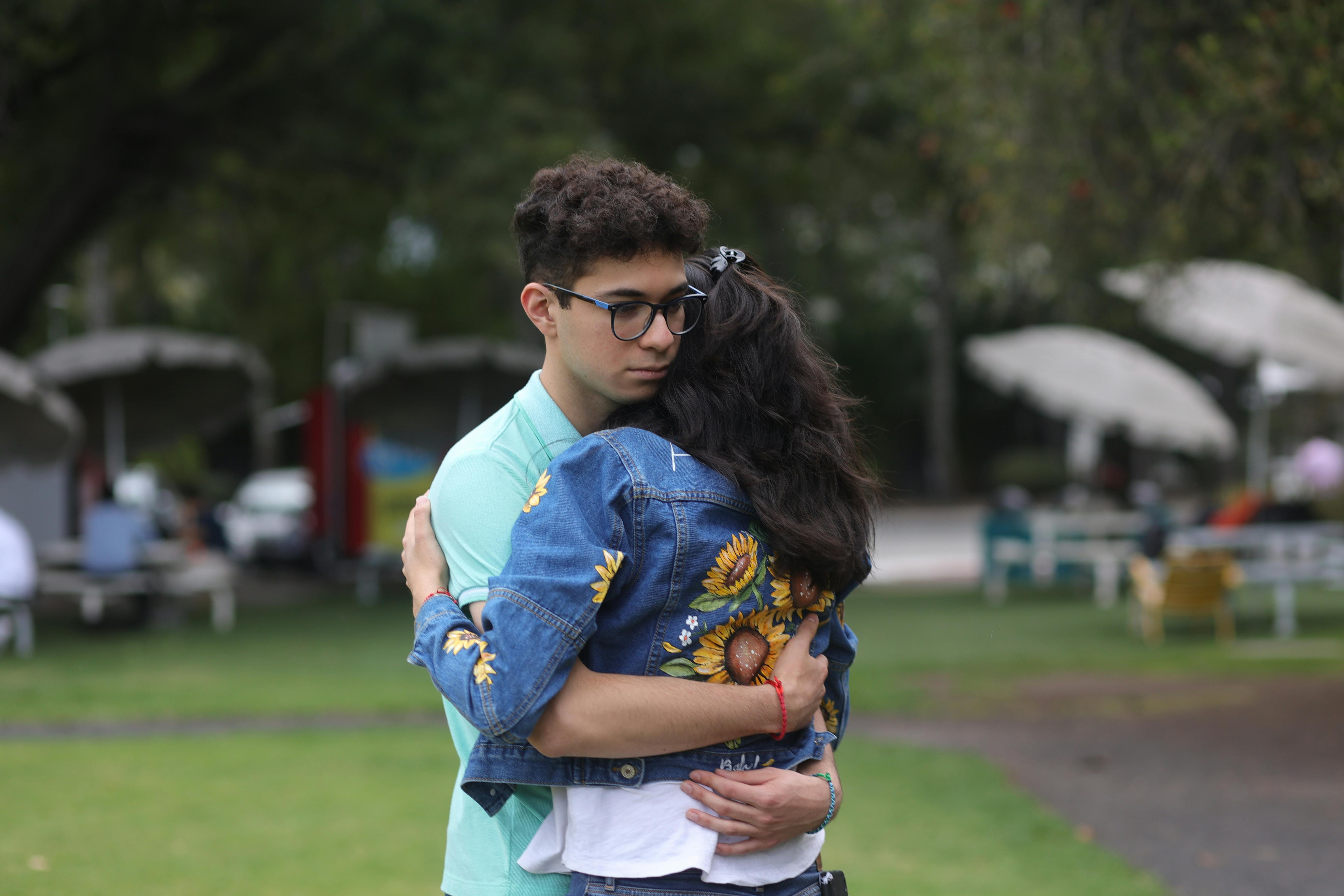 a young man and woman hugging in a park