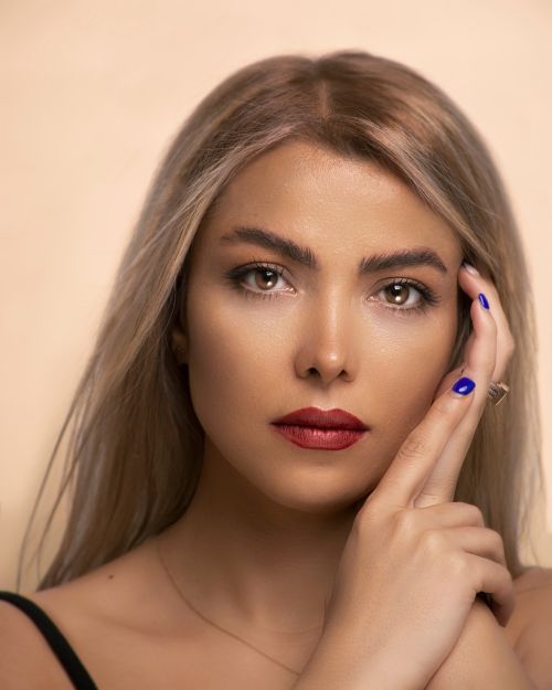 Free Close-up studio portrait of a blonde woman with red lips and blue nails showing elegance. Stock Photo