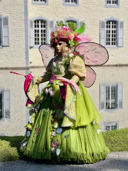 Woman in an elaborate fairy costume poses by a river, reflecting urban elegance.