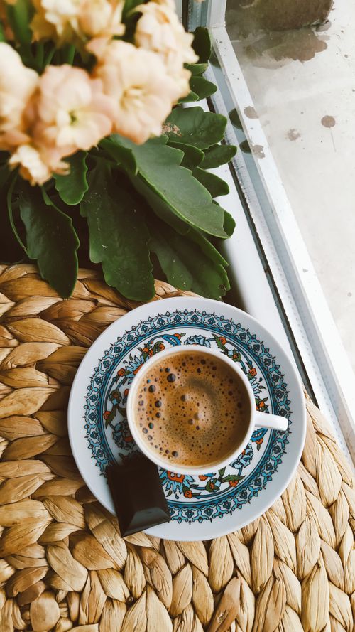 Free A beautifully crafted coffee cup with chocolate by a window, surrounded by plants, offering a cozy atmosphere. Stock Photo