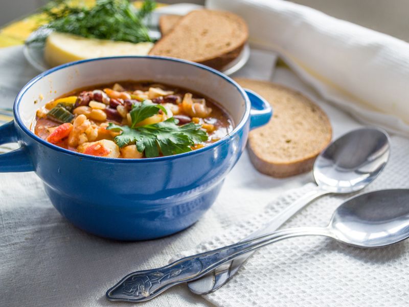 Colorful vegetable soup served in a blue ceramic bowl with bread slices on a cozy table se