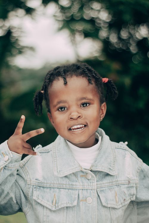 Free A cheerful child with braided hair gesturing in a denim jacket outdoors. Stock Photo
