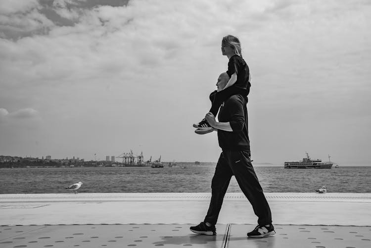 Father Carrying His Daughter On The Shoulders And Walking On The Shore 