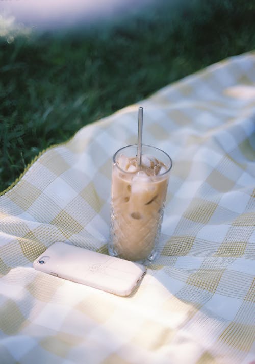 A Glass of Iced Coffee and a Phone on a Picnic Blanket 