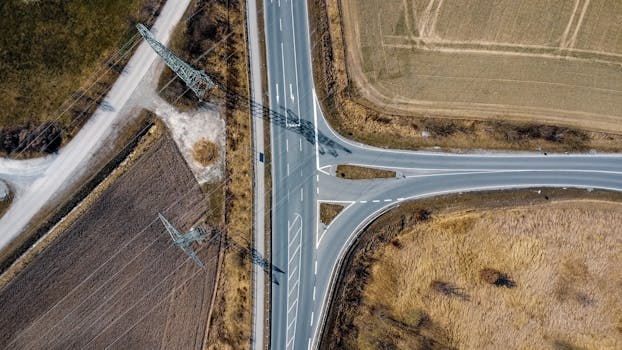 Drone shot capturing a rural road intersection and power lines in Pliening, Germany.