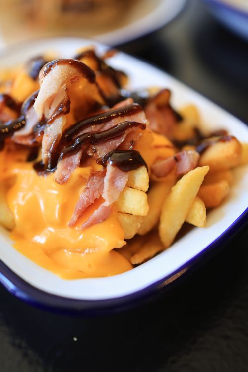 Free Mouthwatering cheese fries topped with crispy bacon and barbecue sauce in a serving dish. Stock Photo
