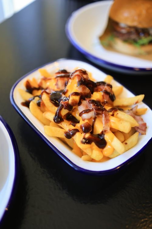 Free Mouth-watering loaded cheese fries topped with bacon and sauce in a casual dining setting. Stock Photo