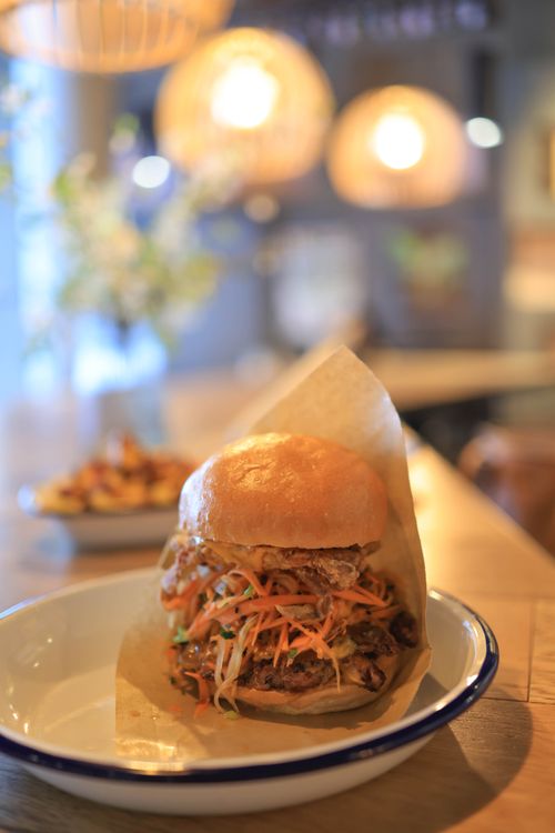 Free A mouthwatering gourmet burger topped with fresh coleslaw served on a rustic plate in a cozy restaurant setting. Stock Photo