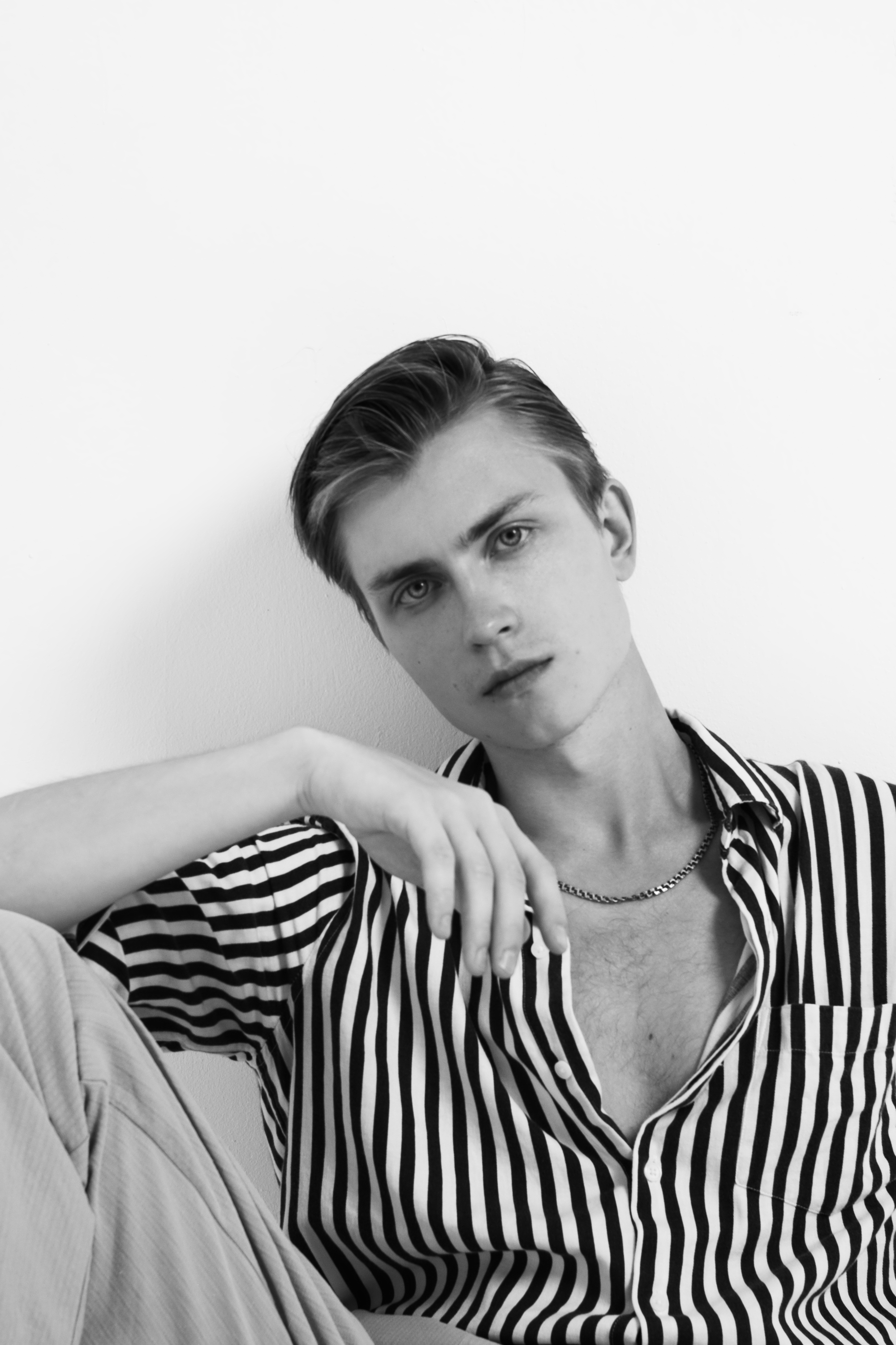 Elegant black and white portrait of a young male in striped fashion attire, posing in studio.