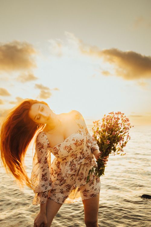 Free Woman enjoying sunset on Turkish shoreline while holding flowers, exuding elegance and tranquility. Stock Photo