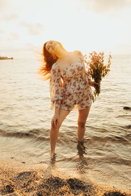 Free Woman in floral dress enjoying sunset on a Turkish beach, holding a bouquet of wildflowers. Stock Photo