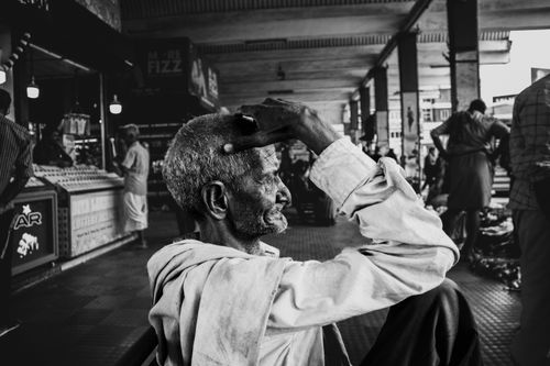 Free Black and white portrait of an elderly man sitting thoughtfully in a bustling urban station. Stock Photo