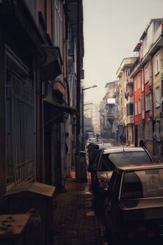 A narrow street filled with parked cars in an old town cityscape, conveying an urban atmosphere.