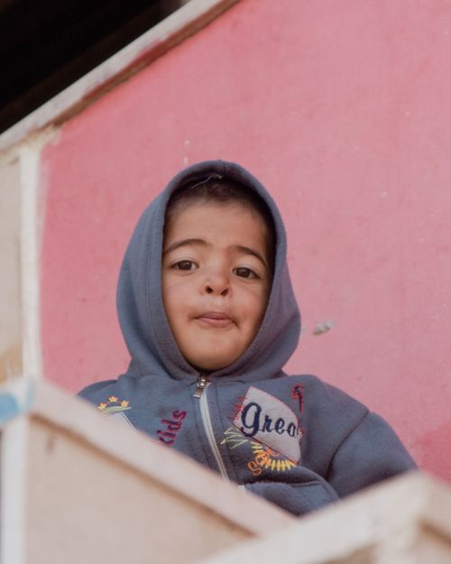 Free Portrait of a young child wearing a hoodie, standing in front of a pink wall. Stock Photo