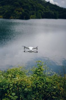 A drone flying above a serene lake with lush greenery, capturing the essence of summer outdoors.