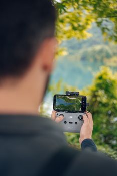 A man using a smartphone and controller to navigate a drone in a lush outdoor setting, offering a tech-savvy perspective.