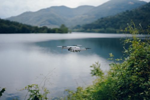 Free Aerial view of a drone flying over a tranquil mountain lake surrounded by lush greenery. Stock Photo