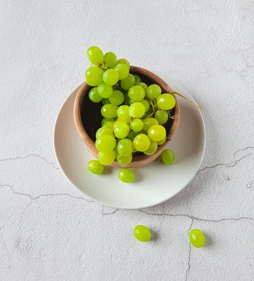 Free Top view of fresh green grapes in a clay bowl on a white plate against a textured surface. Stock Photo