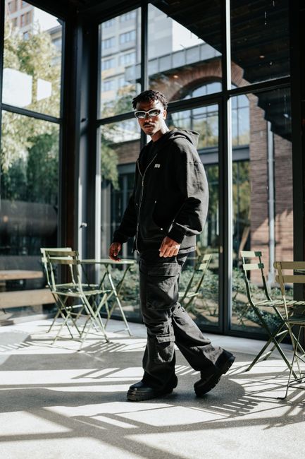 Stylish model in black outfit poses in a trendy sunlit cafe setting.