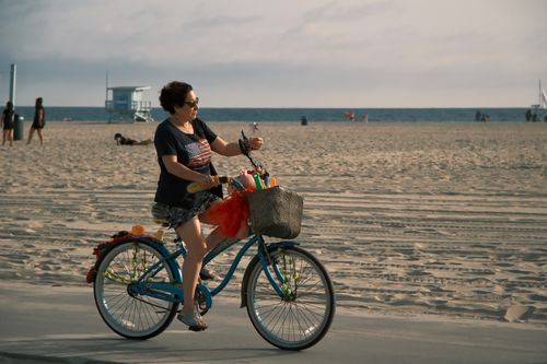 Free A woman enjoying a leisurely bicycle ride on a sunny day along a beachside path. Stock Photo