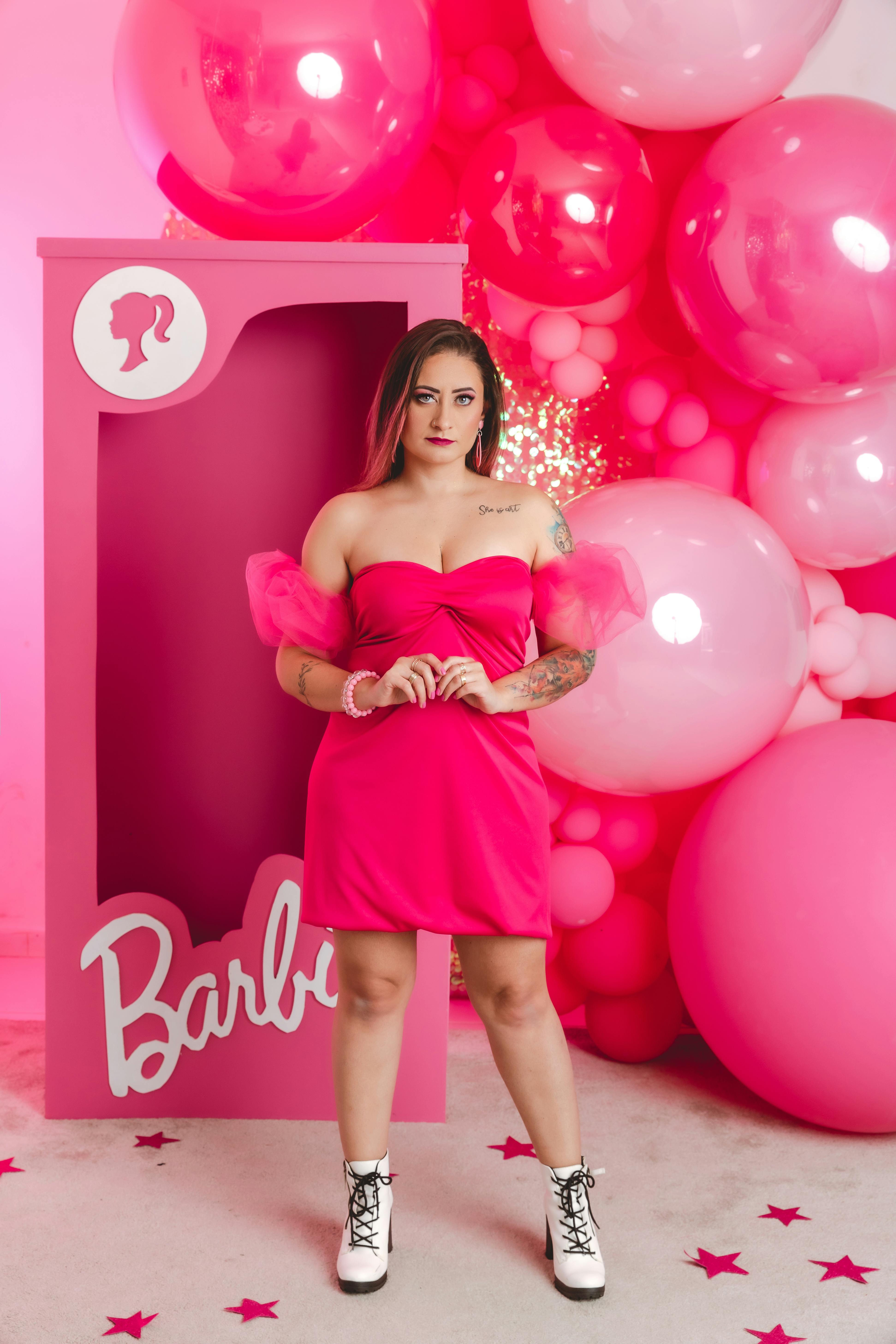 young woman in a pink dress standing on the background of pink balloons and a barbie box