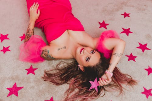 Young Woman in a Pink Dress and Tattoos Lying on the Ground among Star Shaped Confetti 