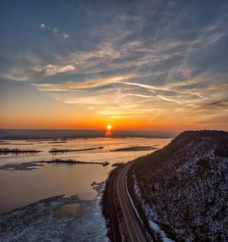 A stunning sunset over the Mississippi River in Minneiska, MN, with a winding road and snow-dusted hill.