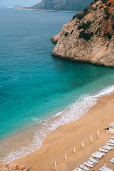 Aerial view of a serene beach in Antalya, Türkiye, featuring loungers and dramatic cliffs.