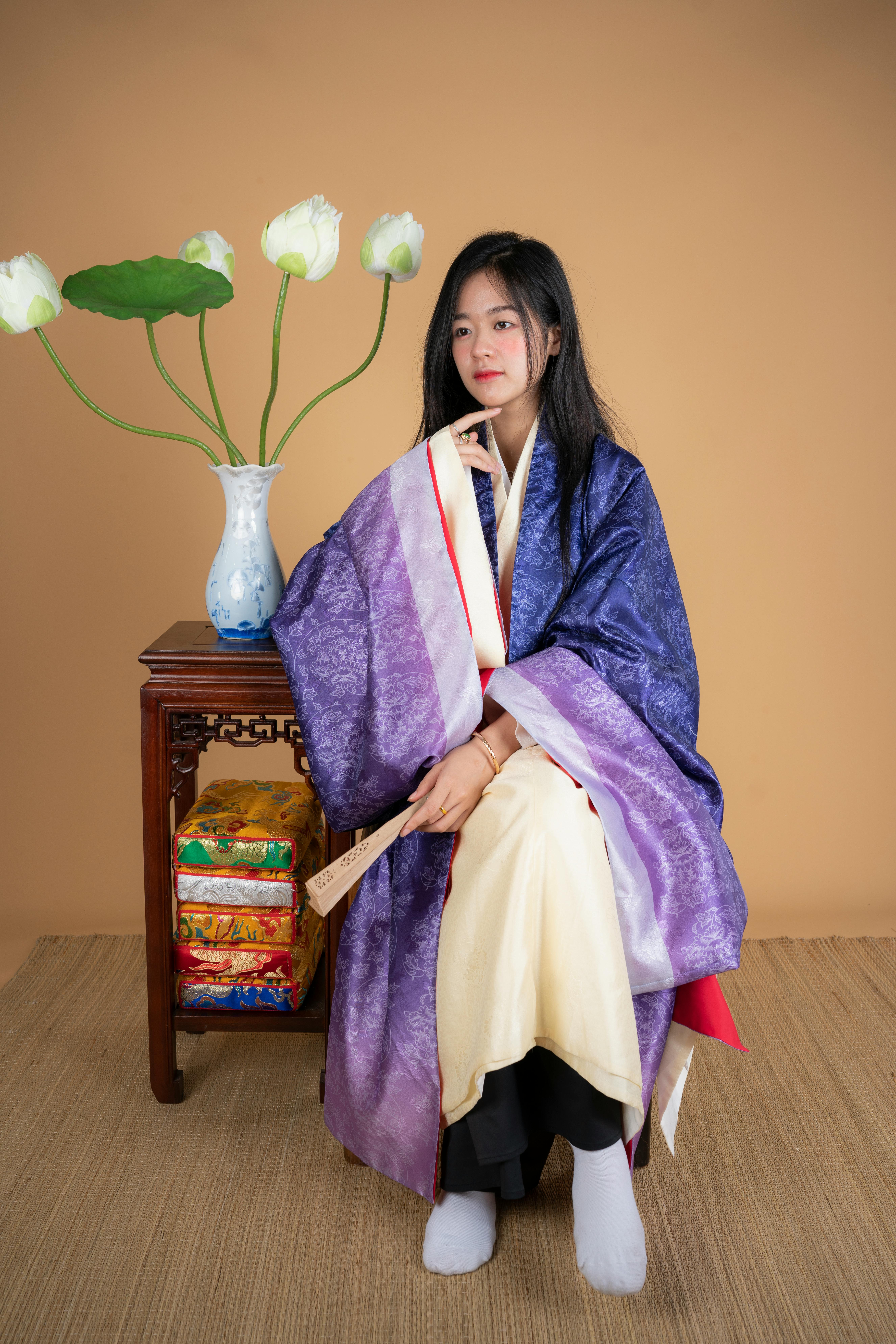 A woman sits gracefully in a kimono, accompanied by a vase and flowers, creating a serene portrait.