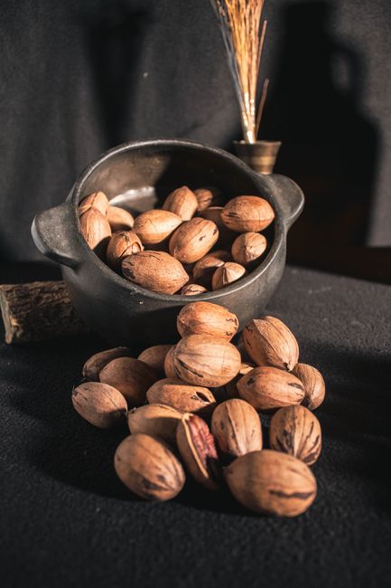 Hồ đào: Hương vị sang trọng, lợi ích bất ngờ 3 A black pot filled with unshelled pecans spilled over a dark fabric creating an artistic composition.