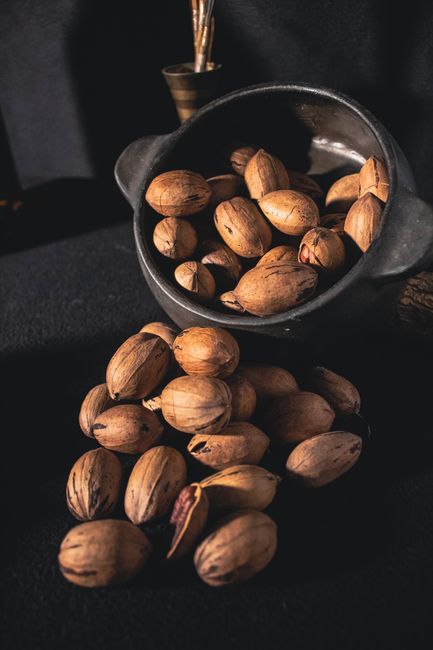 Hồ đào: Hương vị sang trọng, lợi ích bất ngờ 2 A rustic bowl filled with unshelled pecans spilling onto a dark surface, showcasing their organic texture.
