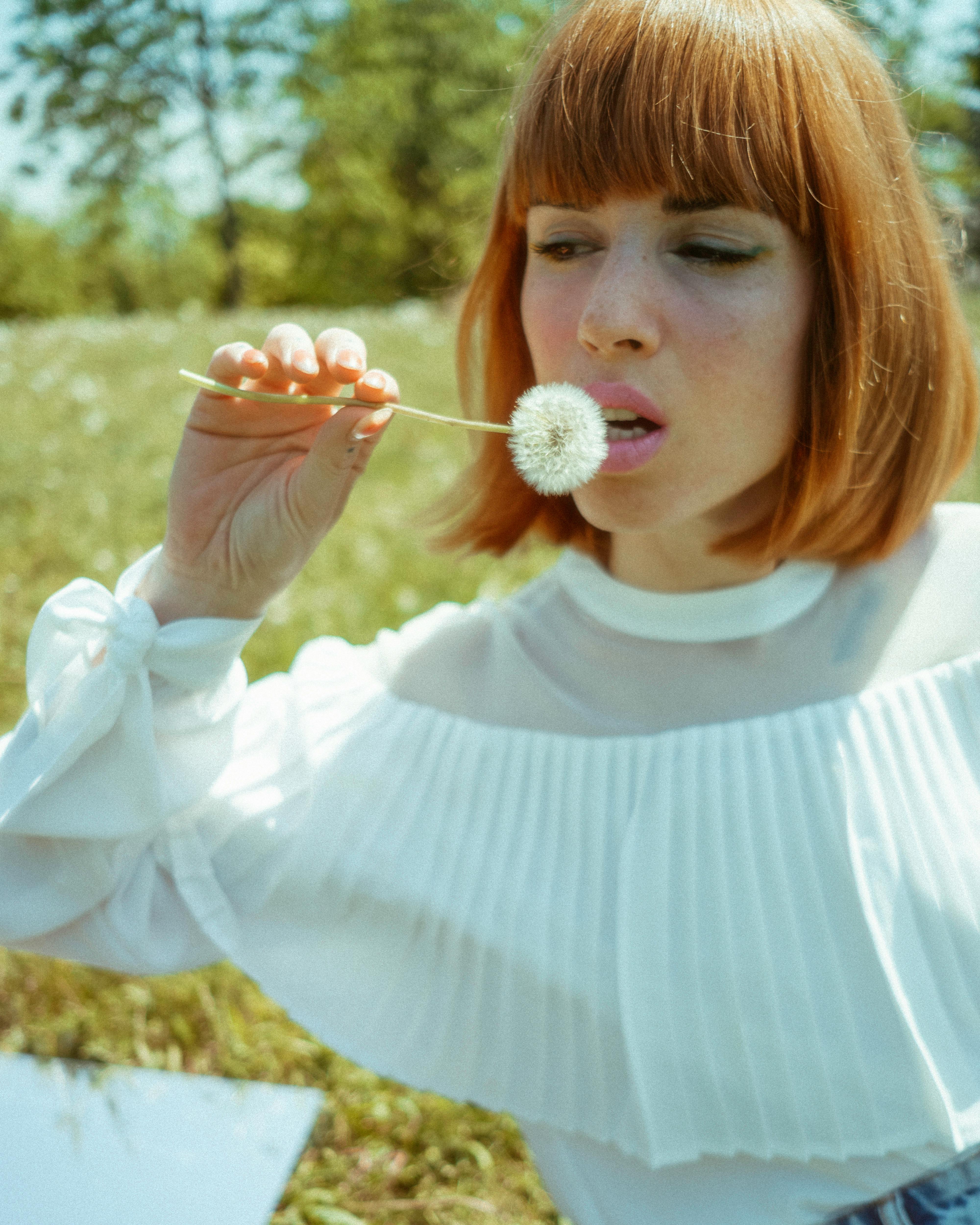 a woman with red hair blowing a dandelion