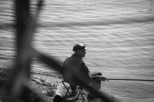 Free Elderly man fishing peacefully on the shore in Liepāja, Latvia, conveying serenity. Stock Photo