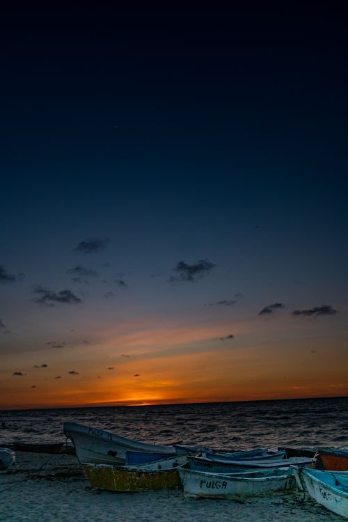 Free Peaceful beach scene at Progreso, Mexico with boats and a vibrant sunset. Stock Photo