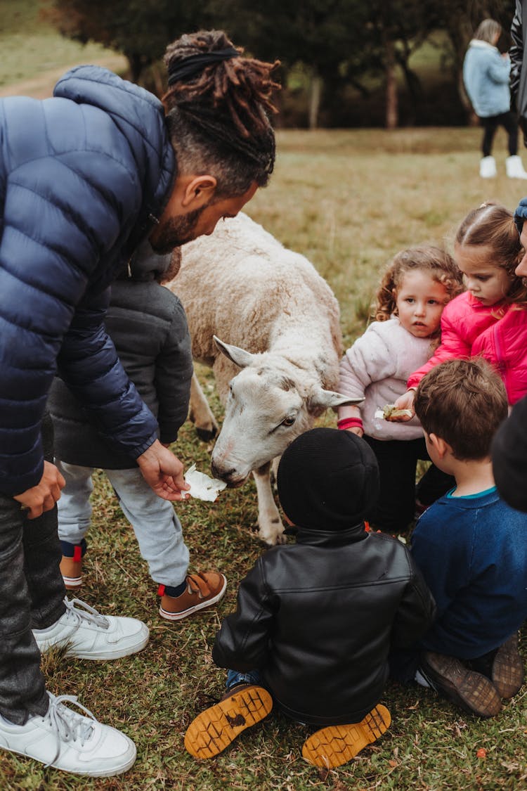 Photo Of A Man Feeding A Sheep Surrounded By A Group Of Children