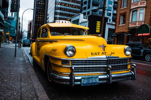 Classic yellow taxi parked on urban street with tall buildings, showcasing retro charm.